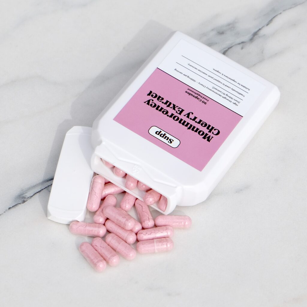 Supp Montmorency Cherry Extract laid on marble table with capsules next to it