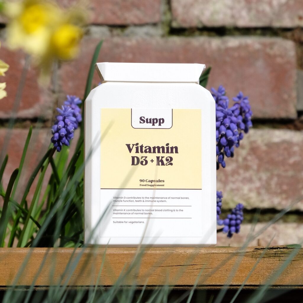 Supp vitamin D3 + K2 next to flowers outside.