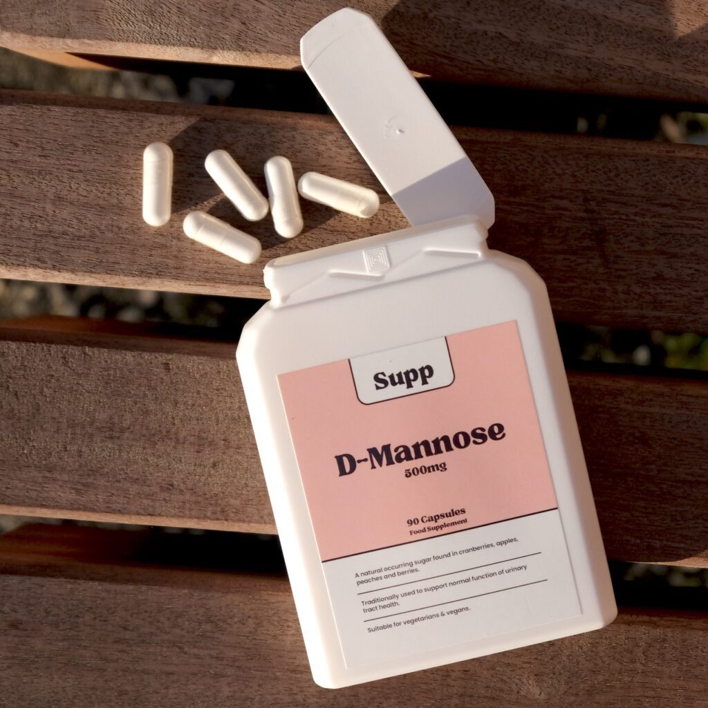 A bottle of Supp D-Mannose has capsules spilling out onto a wood background.
