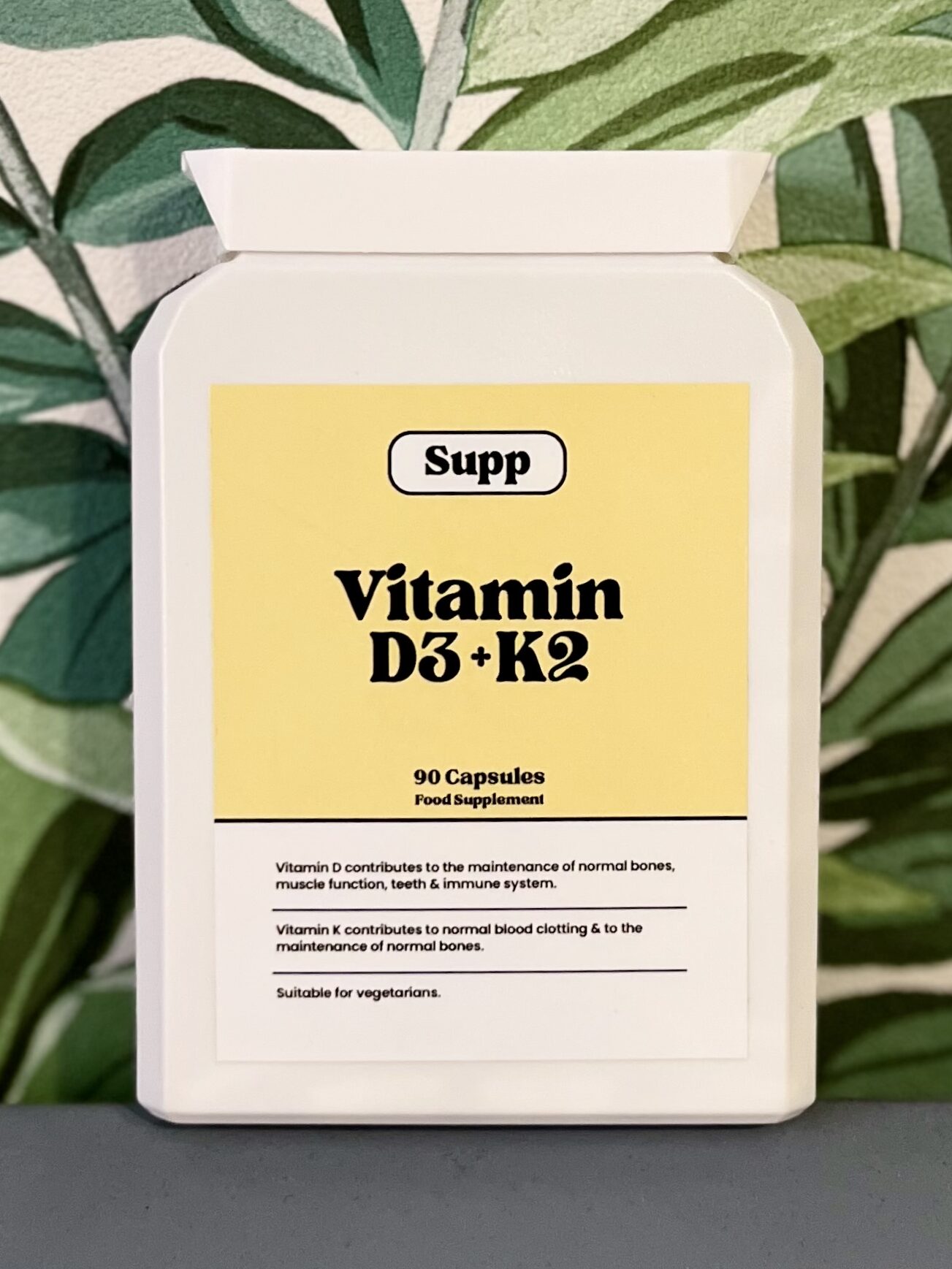 Supp Vitamin D3 & K2 bottle with a tropical plant wallpaper background.