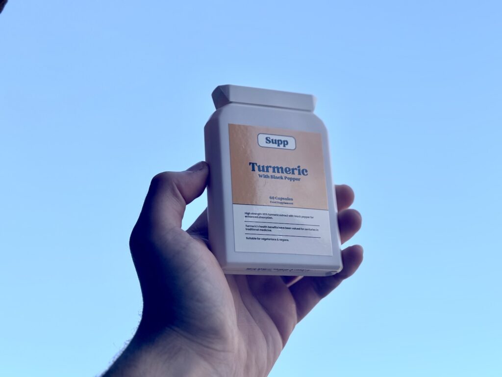 a man's hand holding up supp turmeric extract bottle against a blue sky