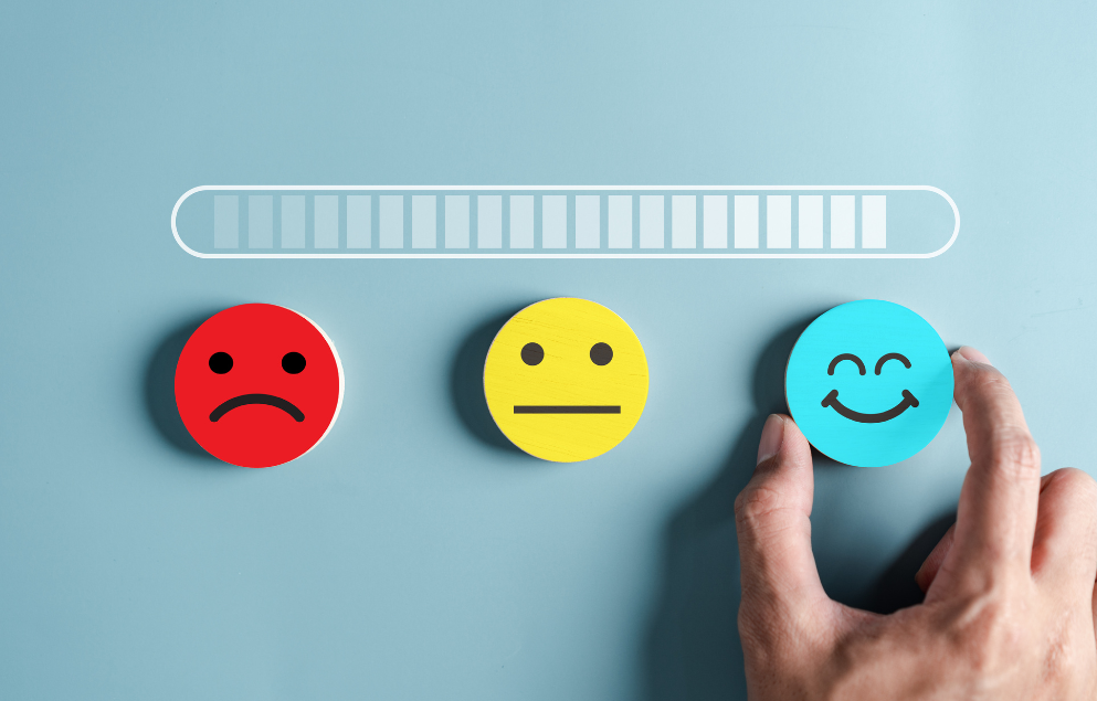 Hand selecting a blue happy face icon from three options—red sad face, yellow neutral face, and blue smiling face—with a progress bar above, symbolising getting happier.
