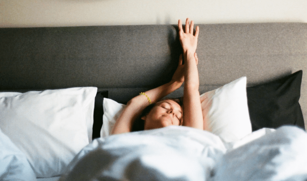 Woman peacefully waking up and stretching in bed, looking rested and relaxed.