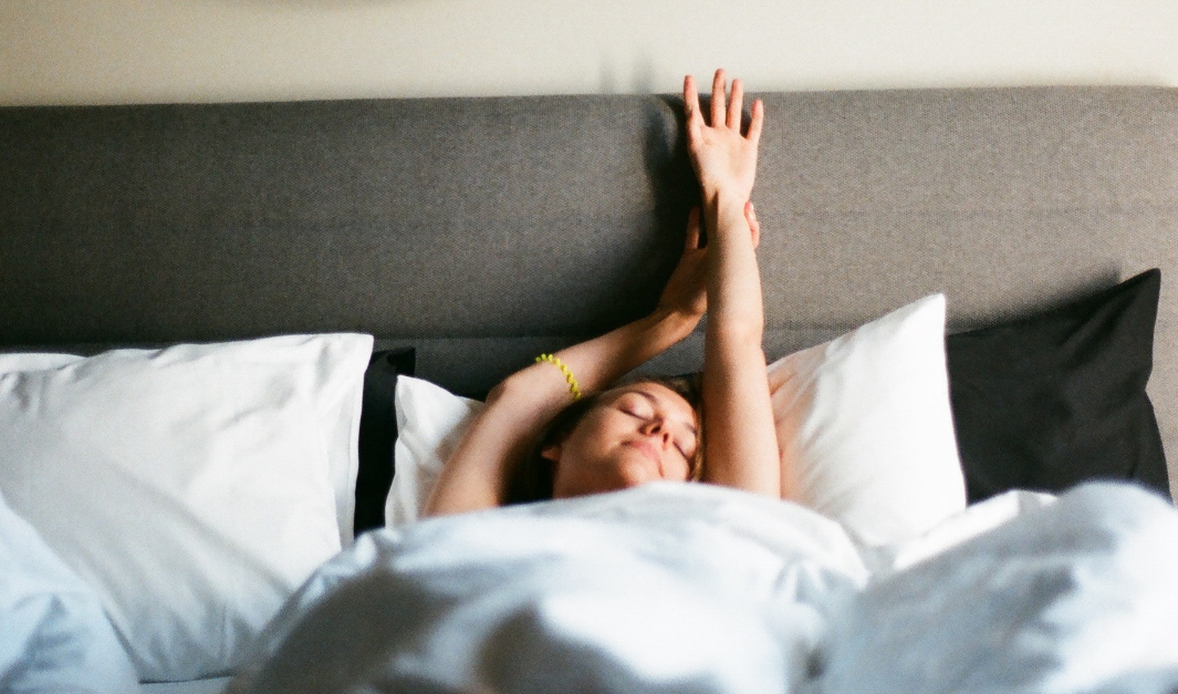 Sleeping Woman peacefully waking up and stretching in bed, looking rested and relaxed.