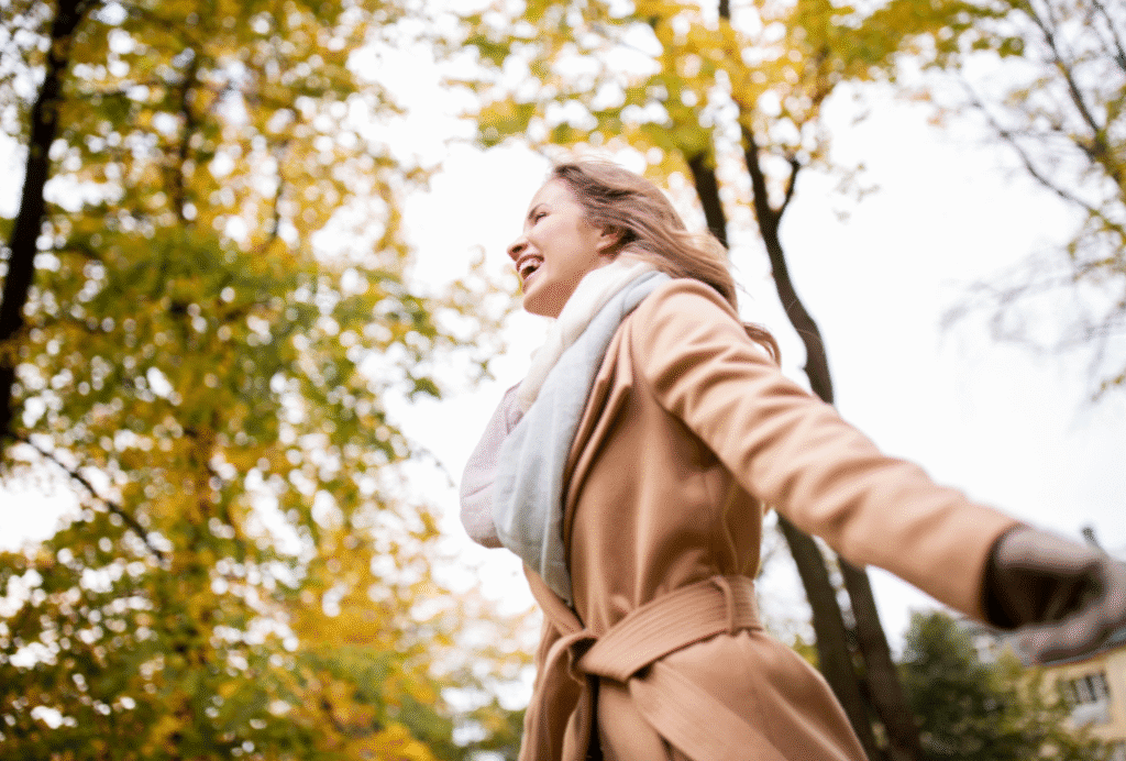 Woman relieving stress with a refreshing autumn walk outdoors, surrounded by trees and falling leaves.