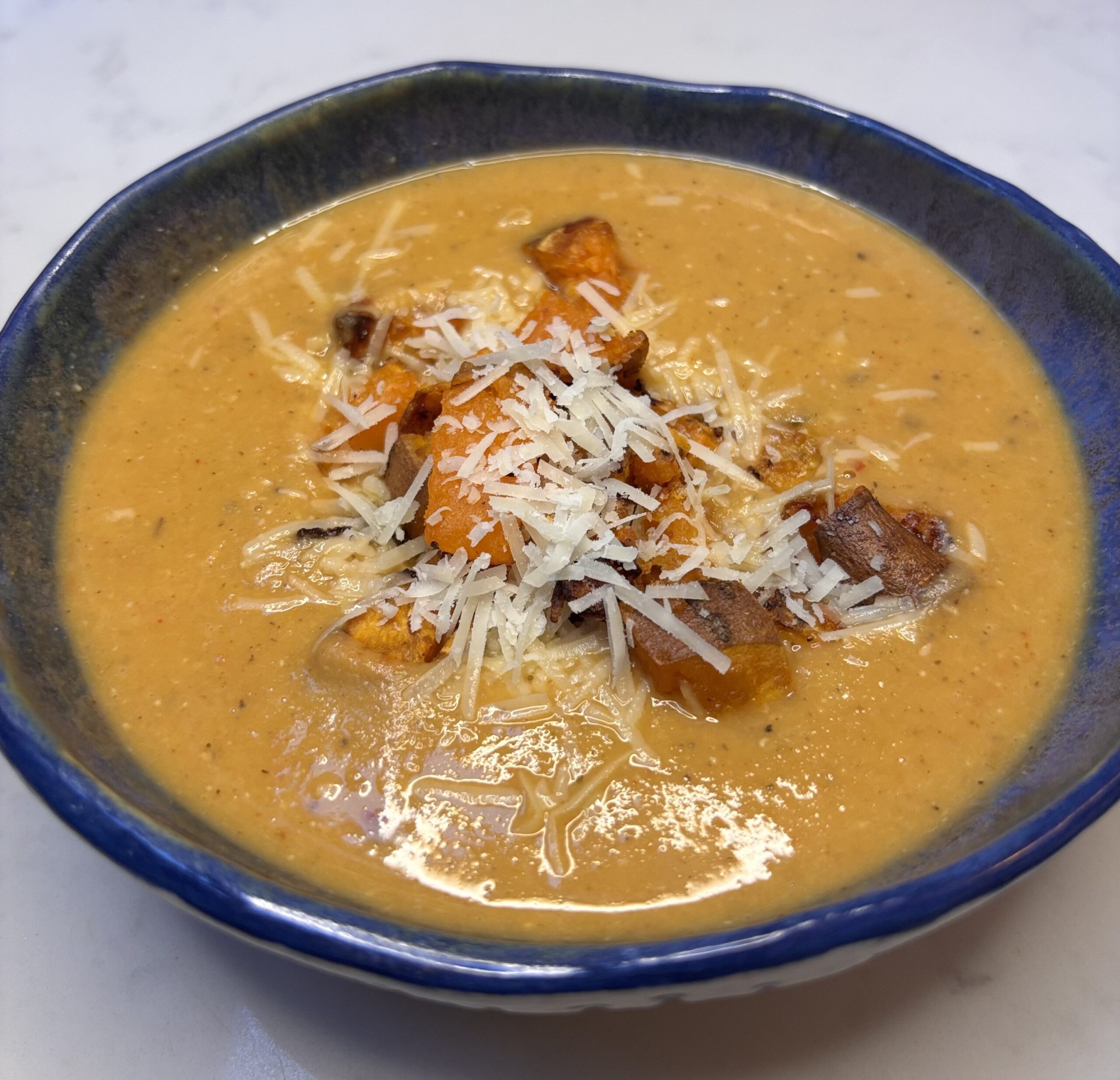 A bowl of tomato and lentil soup topped with sweet potato croutons and parmesan cheese.