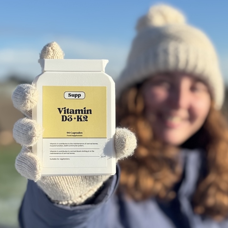 Olivia holds a bottle of Supp vitamin D in the winter sun close up.