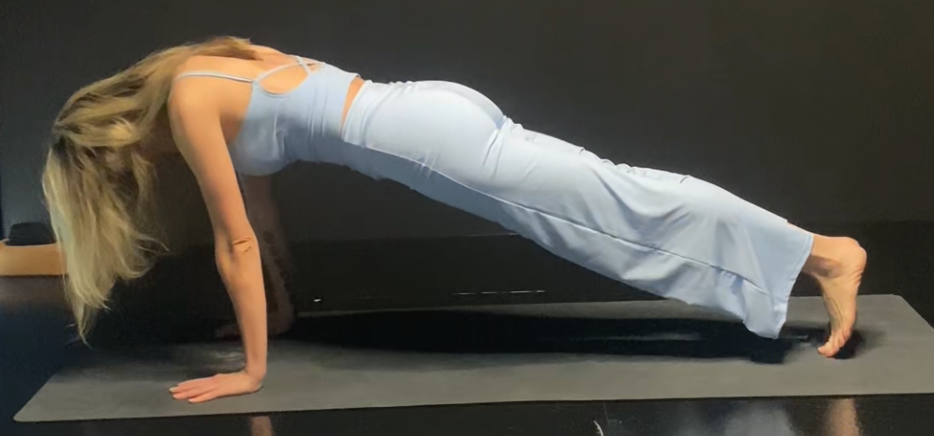 A woman performing plank pose, engaging the core, on a yoga mat.