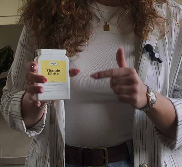 A81F76BF-D440-4713-840C-74502BD24AD3 A woman pointing to a vitamin D supplement bottle, ready to answer the question - How much vitamin D should you be taking in the uk?
